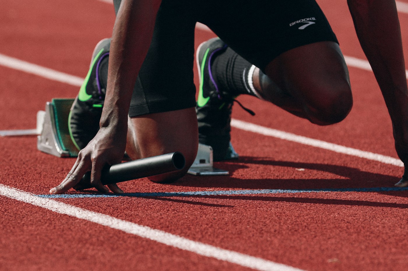 Sprinter in starting blocks holding a baton